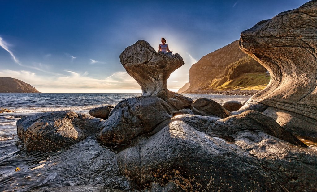 Mulher em meditação no alto de uma pedra cercada de montanhas e do mar