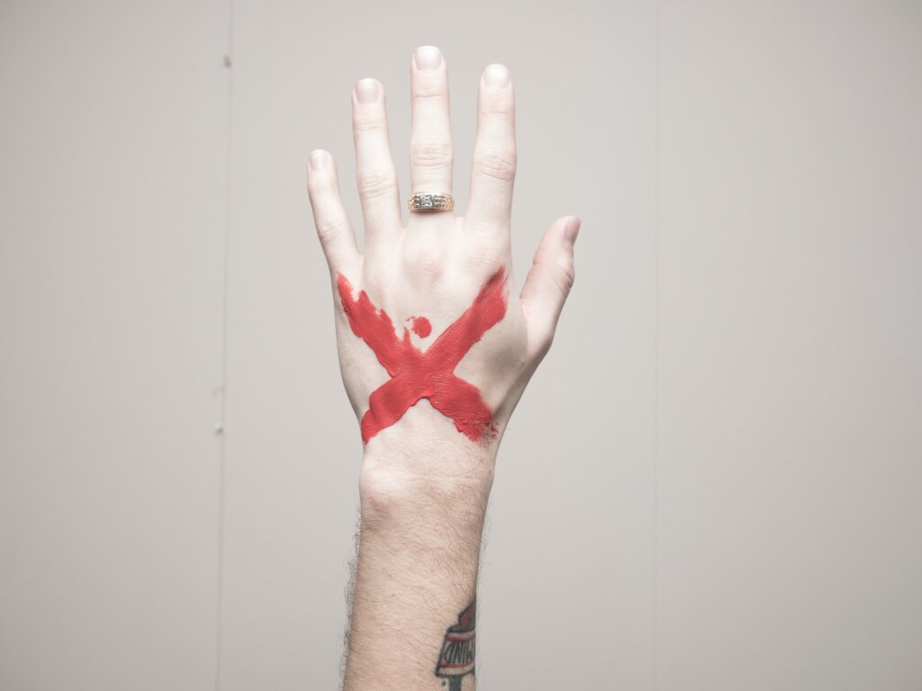 Mão de um homem com anel e um x vermelho no meio